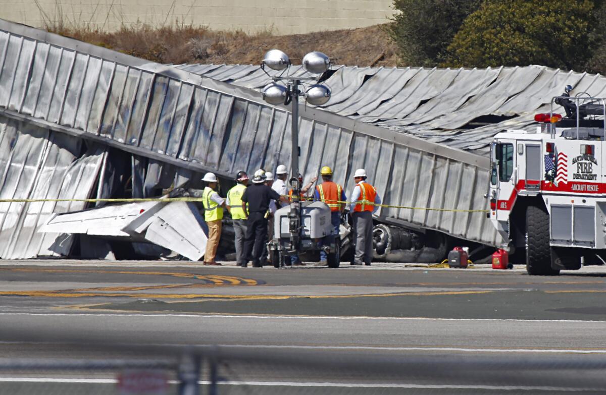 Investigators stand near the tail section of the twin-engine plane that crashed Sunday outside a hangar at Santa Monica Airport.