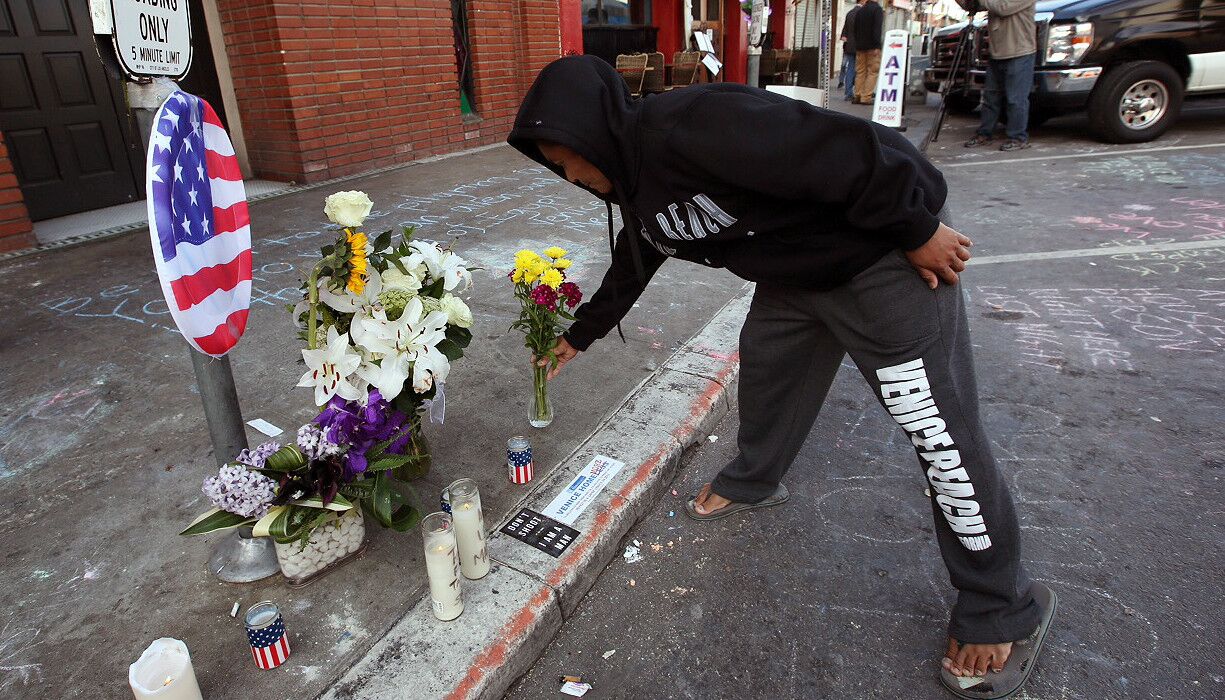 A man places flowers at a growing memorial for a homeless man killed by LAPD in Venice.