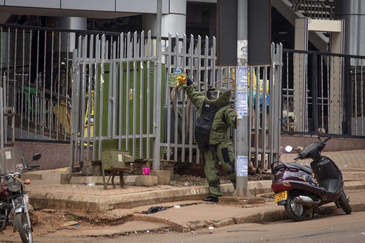 A bomb disposal officer examines a suspicious package resembling a gift before subjecting it to a controlled explosion, next to the central police station in Kampala, Uganda, Tuesday, Nov. 16, 2021. Two loud explosions rocked Uganda's capital, Kampala, early Tuesday, sparking chaos and confusion as people fled what is widely believed to be coordinated attacks. (AP Photo/Nicholas Bamulanzeki)