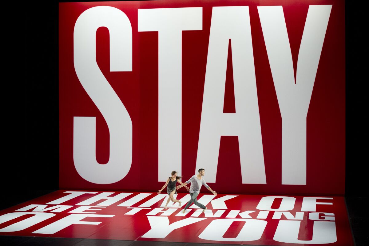 Two dancer on a stage wrapped in red vinyl with large white letters reading "STAY" and "Think of me thinking of you"