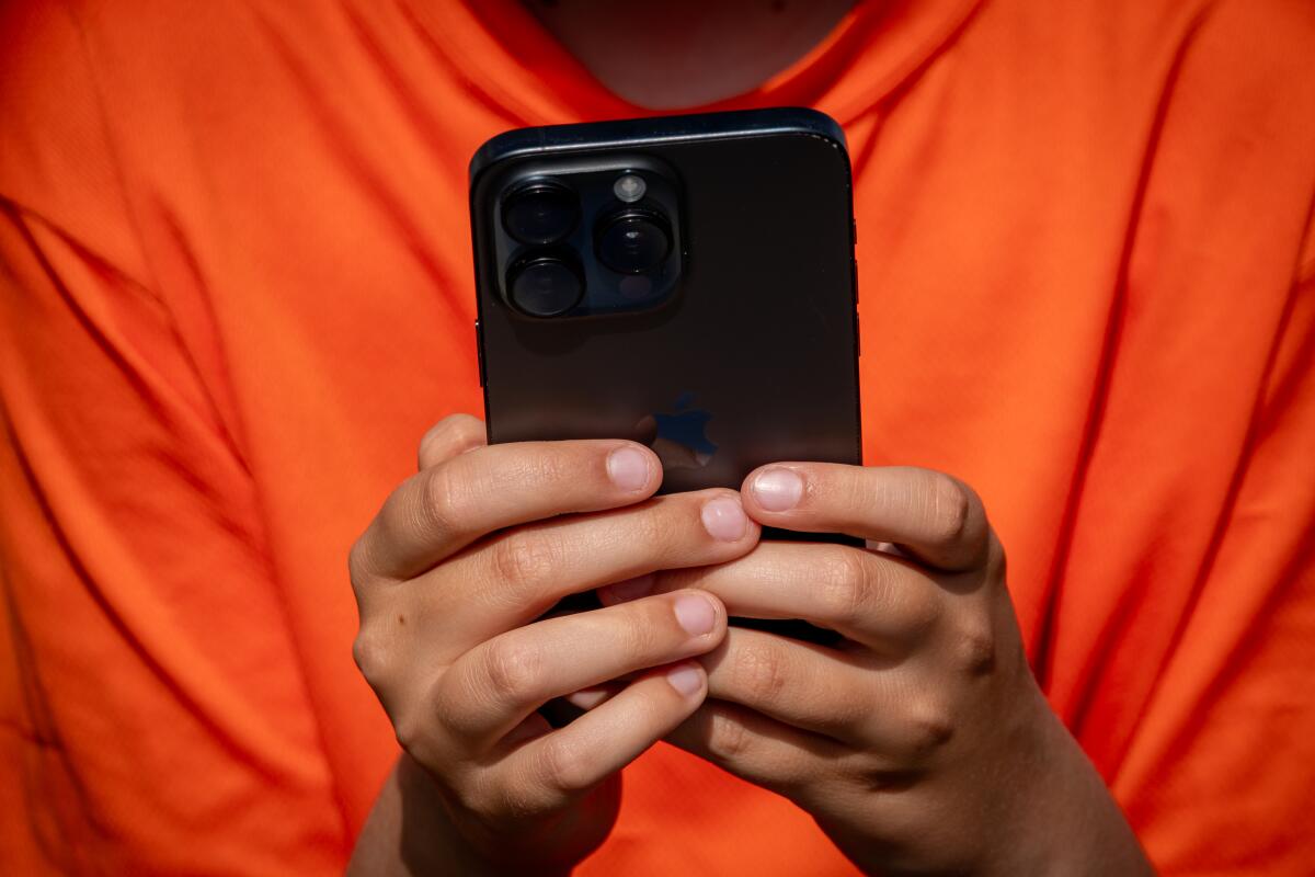 A boy in an orange shirt holidng a cell phone 