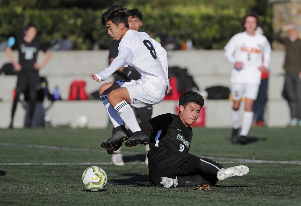 Huntington Beach senior Justin Fujimori takes control of the ball, avoiding a slide from Costa Mesa senior Marco Castrejon in the first half of a Hawks Invitational pool-play match at Lake Forest Sports Park on Friday.