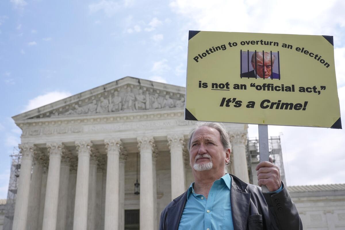 A demonstrator stands outside the Supreme Court with a sign picturing Donald Trump behind bars.