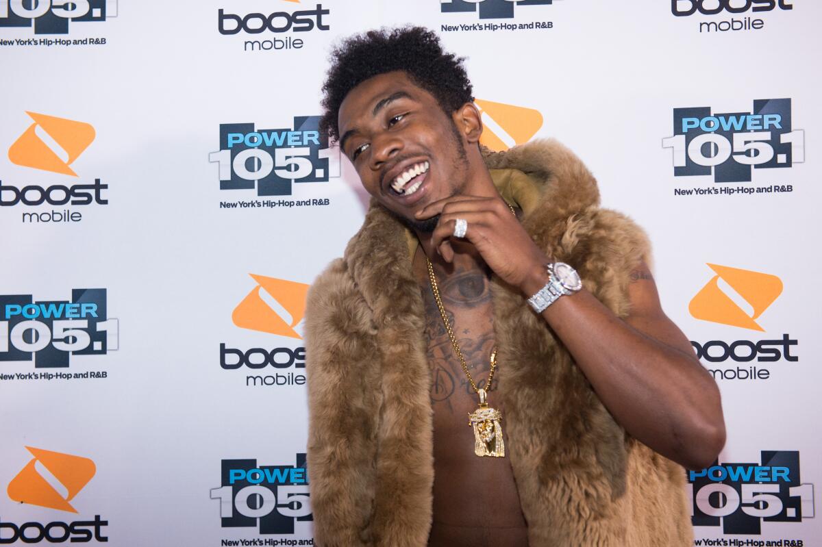Rapper Desiigner smiling with hand under his chin while wearing a fur vest and gold chain.