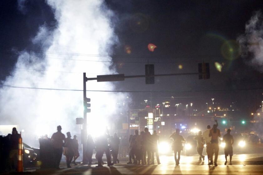 People stand near a cloud of tear gas during summer protests in Ferguson, Mo.