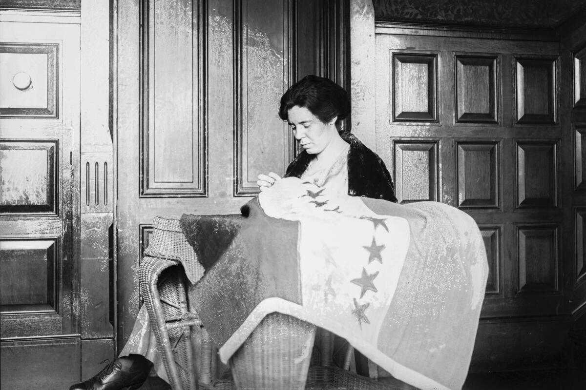 A woman looks down as she sews a flag bearing stars