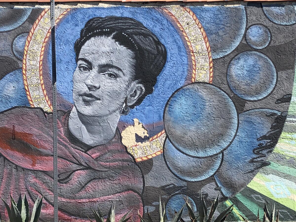 A mural shows an image of a gently smiling Frida Kahlo against a cosmic blue background.