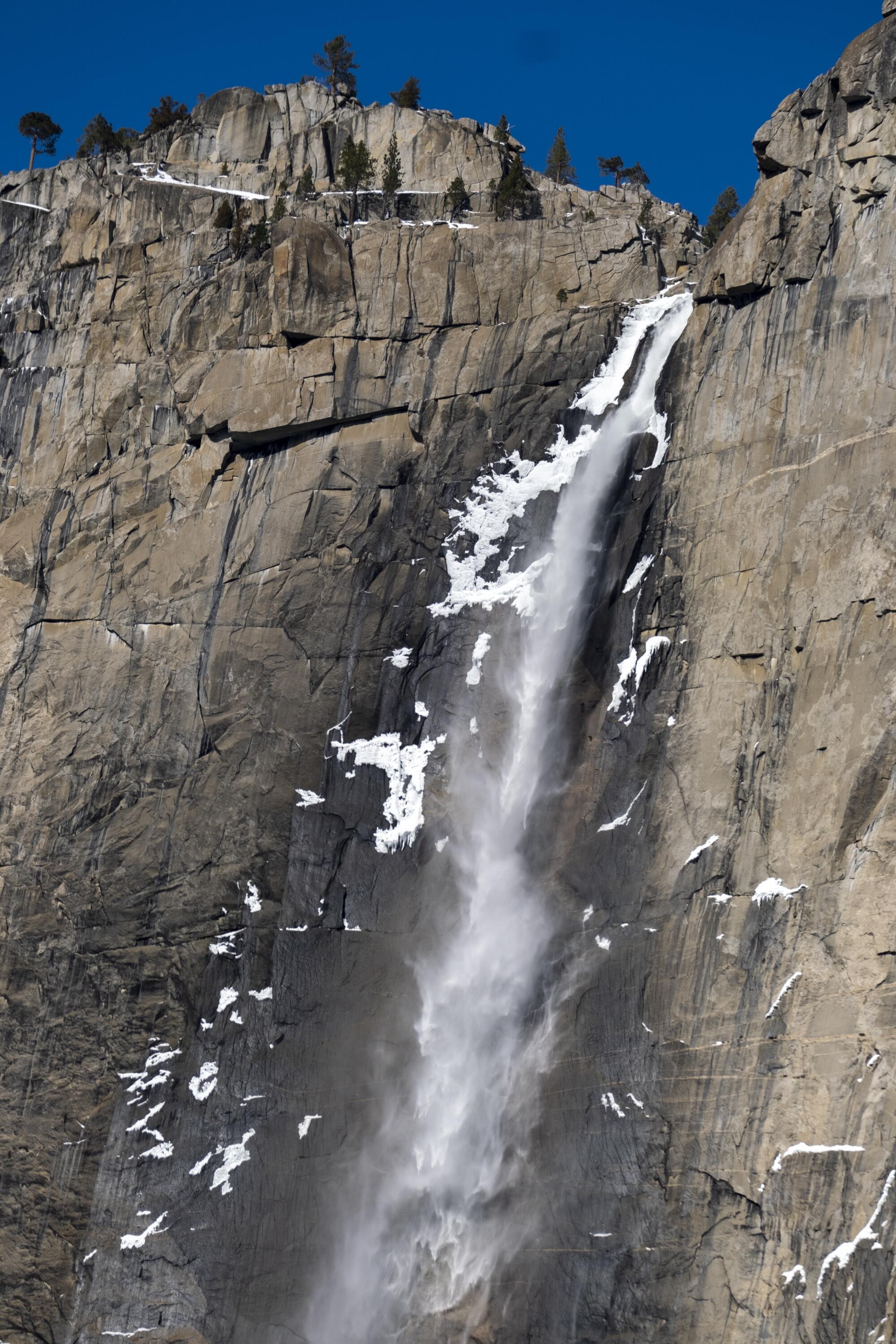 A waterfall plummets down a granite prominence marked by patches of snow and ice.