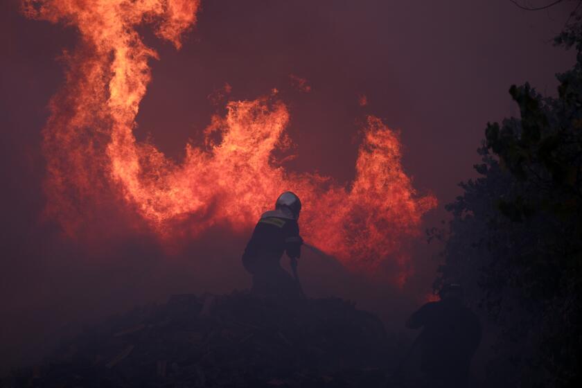 A firefighter tries to extinguish the flames at a business during a fire in northern Athens, Monday, Aug. 12, 2024, as hundreds of firefighters tackle a major wildfire raging out of control on fringes of Greek capital. (AP Photo/Aggelos Barai)