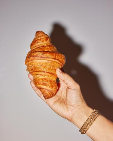 A hand holds up a croissant