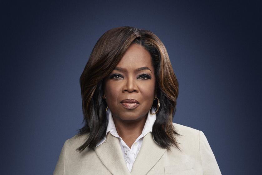 Oprah Winfrey in a beige suit before a deep blue backdrop