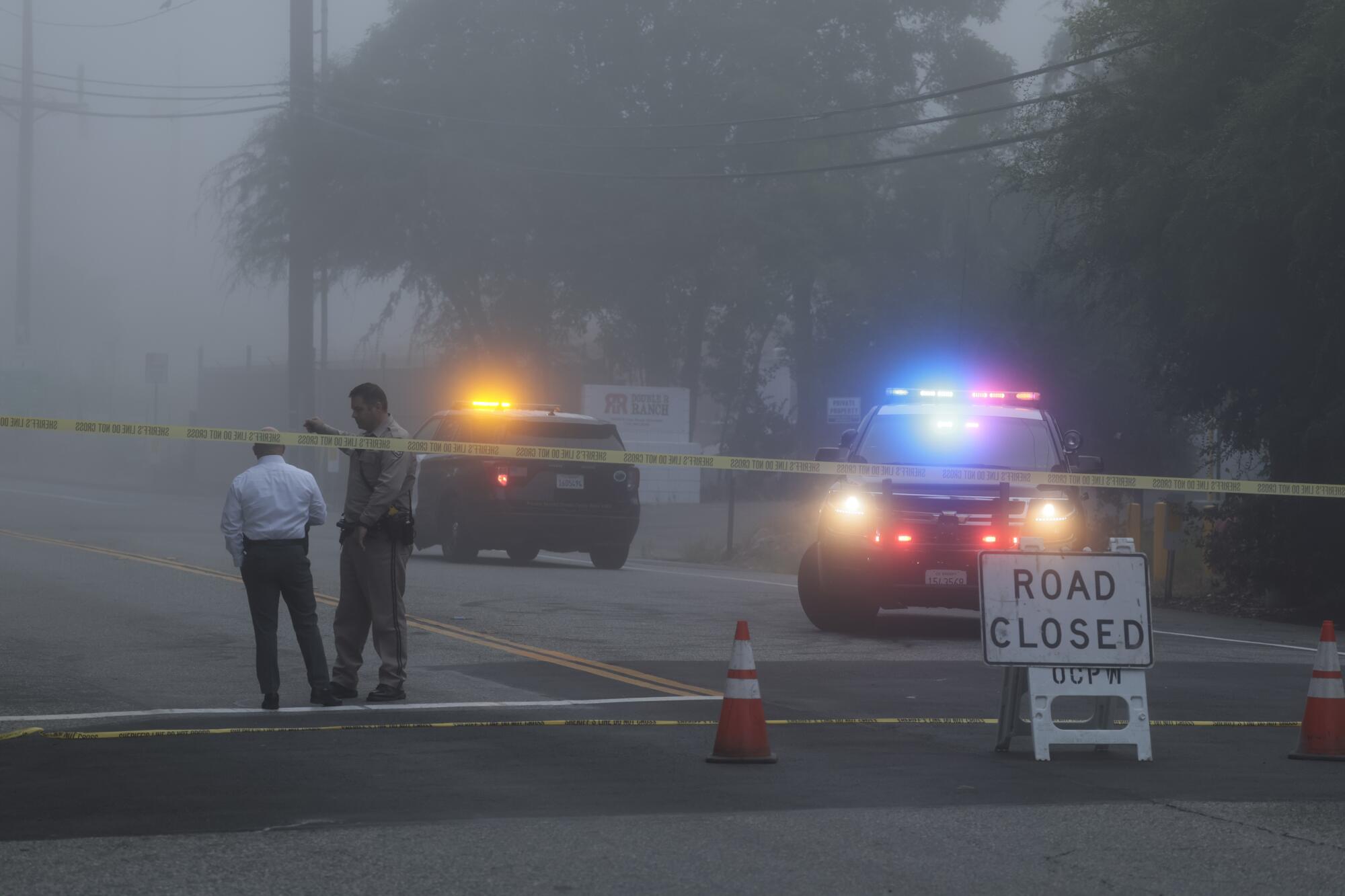 Fog blankets a roadway on which law enforcement vehicles are parked.