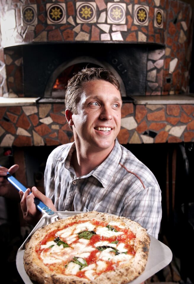 Settebello owner Brad Otton holds a pizza in front the pizzeria's 900-degree domed wood-fired oven.