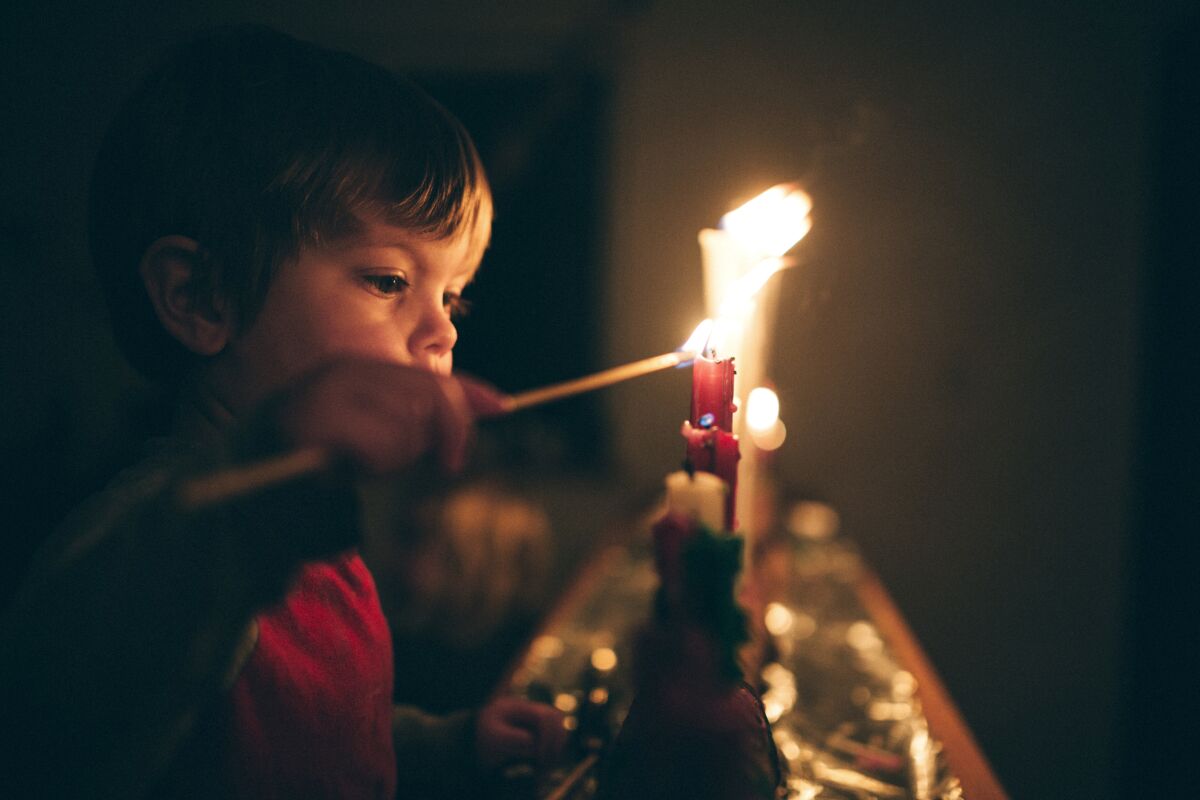 Un simpático niño enciende una hilera de velas para el tiempo de Adviento