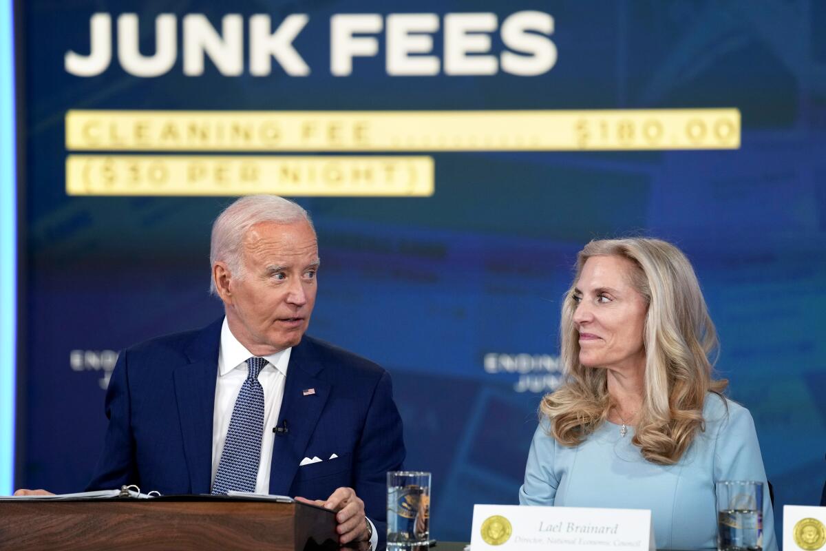 President Joe Biden speaks seated at left, next to Lael Brainard, while they look at each other.