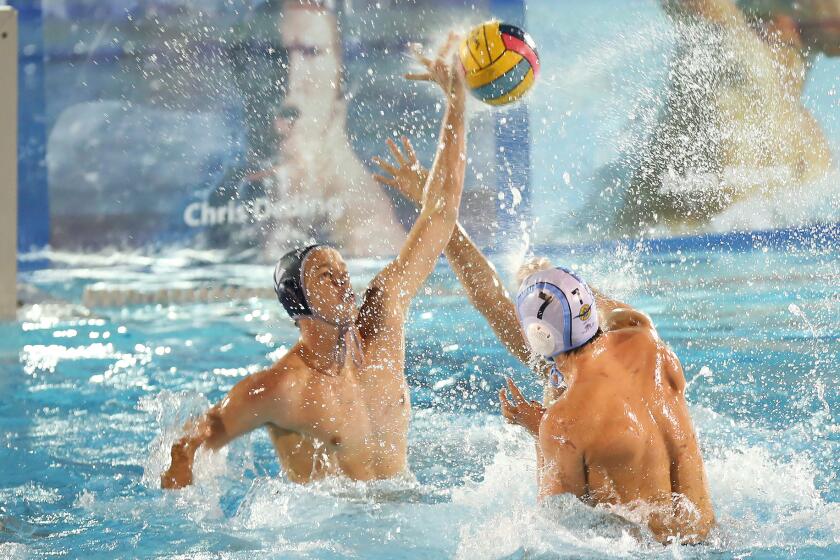 Newport Harbor's Tommy Kennedy (12) blocks the long shot by Corona del Mar's Tanner Pulice (7) during Battle of the Bay water polo match on Wednesday.