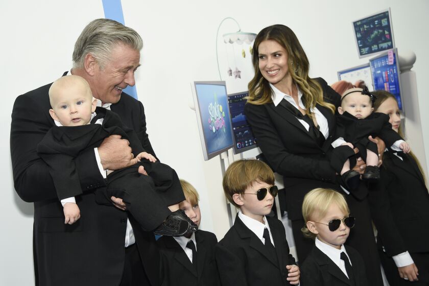 A man and a woman posing in matching black suits with a bunch of kids