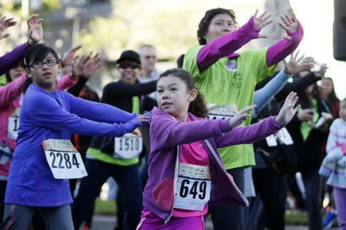 Carly Gallegos, 7 of Palmdale, center, braved to cold and warmed up before running in the 6th annual Glendale News-Press 5K Downtown Dash & Walk on Brand Boulevard in Glendale on Sunday.