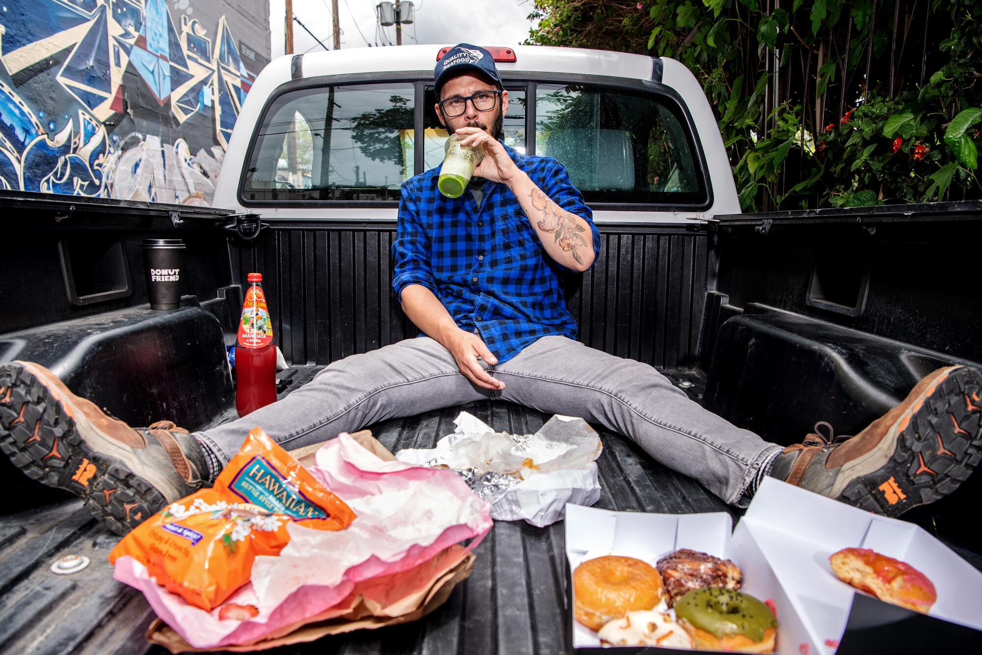 Portrait of Danny Palumbo sitting in the back of his truck, surrounded by food and drinking some green juice. 