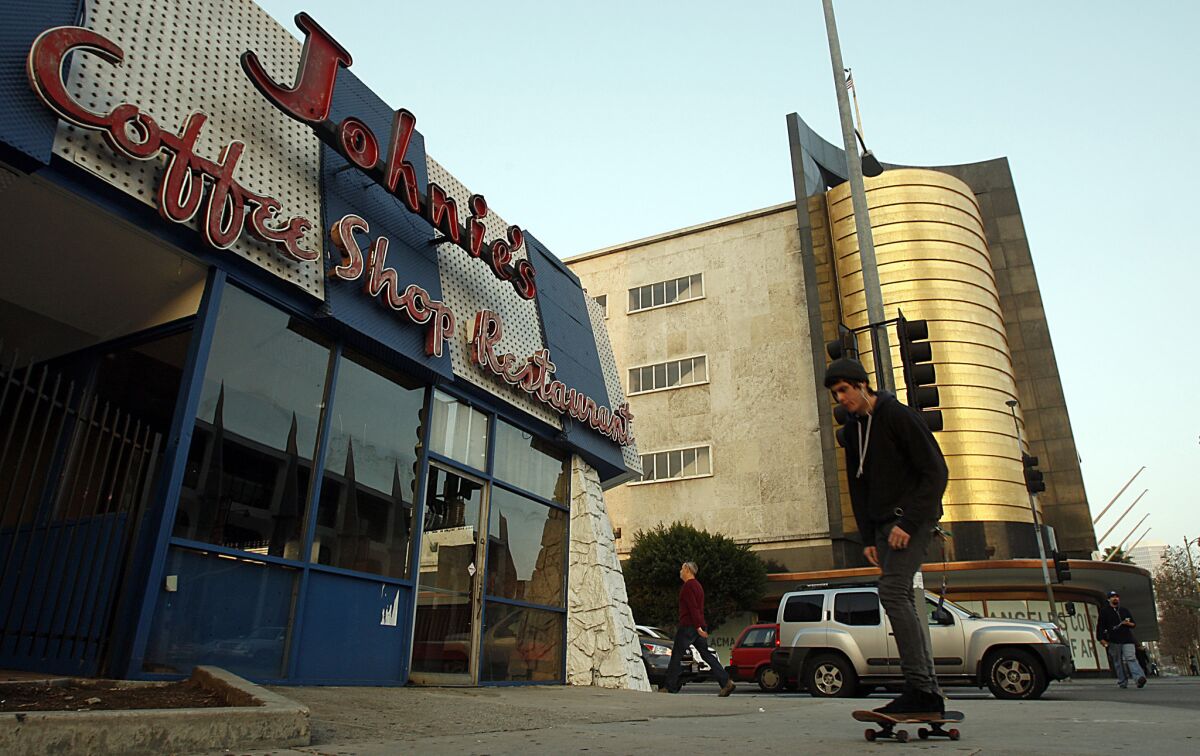 A skateboarder passes Johnie's Coffee Shop and the former May Co. department store on Wilshire Boulevard.