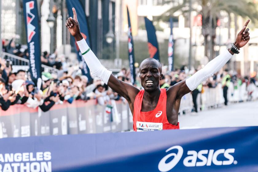 Dominic Ngeno raises his arms as he crosses the finish line, winning the elite male division of the 39th L.A. Marathon