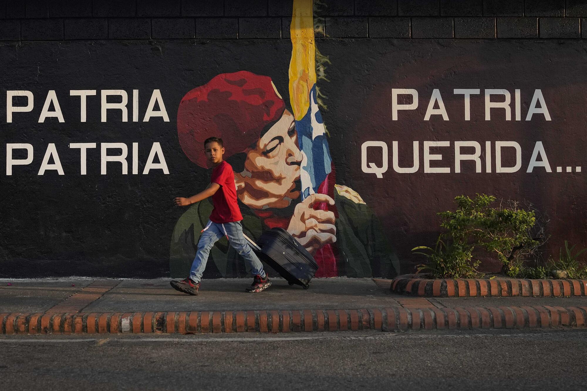 A boy walks past a mural of a man in a red beret kissing a yellow, blue and red flag.