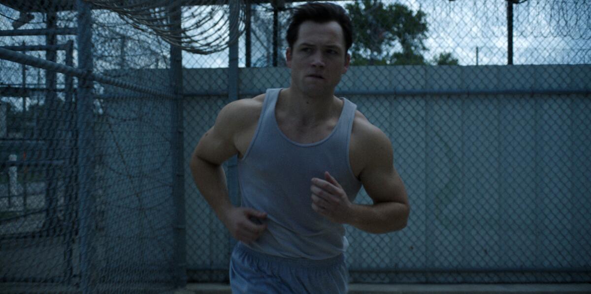 A man in a gray tank top exercises in a prison yard