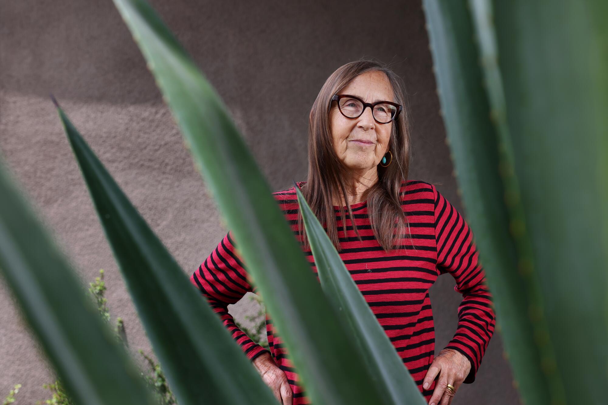 Michelle Huneven, in a red and black striped shirt, stands behind a large succulent.