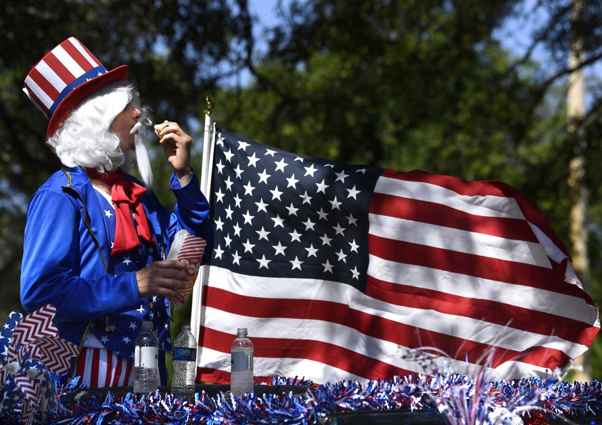 A person dressed as Uncle Sam stands near an American flag outdoors.
