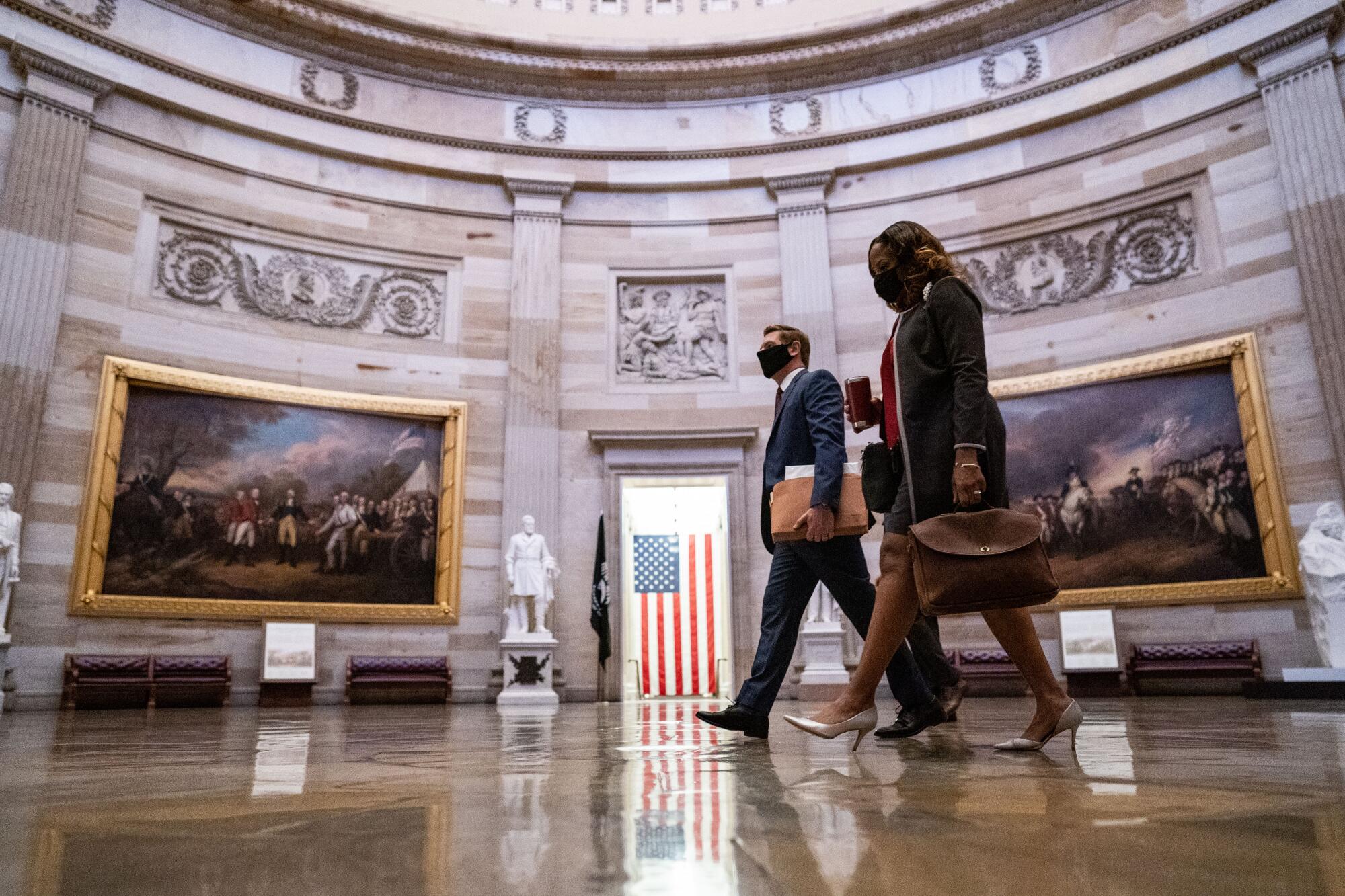 Rep. Eric Swalwell and Rep. Stacey Plaskett wear masks as they cross the Capitol Rotunda.