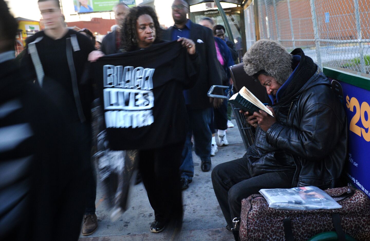 Protesters walk by a homeless man reading a book on Crenshaw Boulevard on Monday.