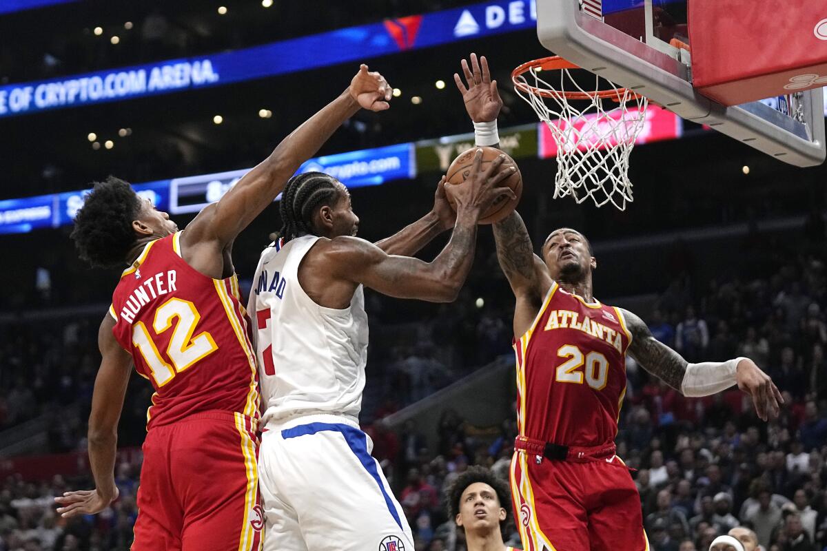 Clippers forward Kawhi Leonard, center, shoots as Atlanta Hawks forwards De'Andre Hunter, left, and John Collins defend.