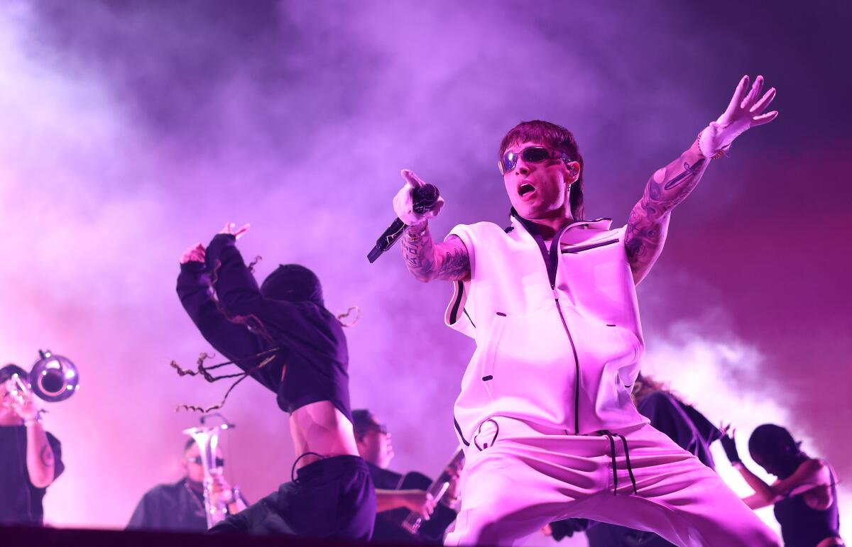 Peso Pluma performs at Coachella with other performers and colored smoke in the background.