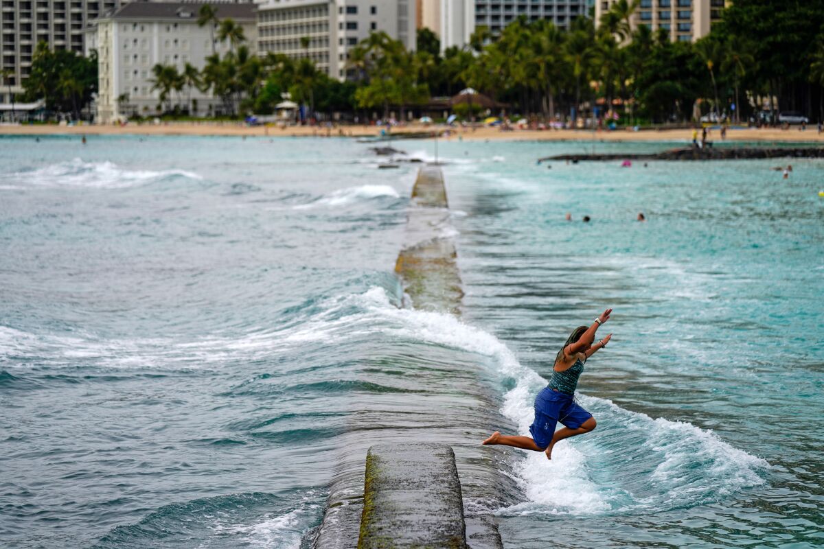 A young woman leaps from the sea wall off Waikiki Beach.