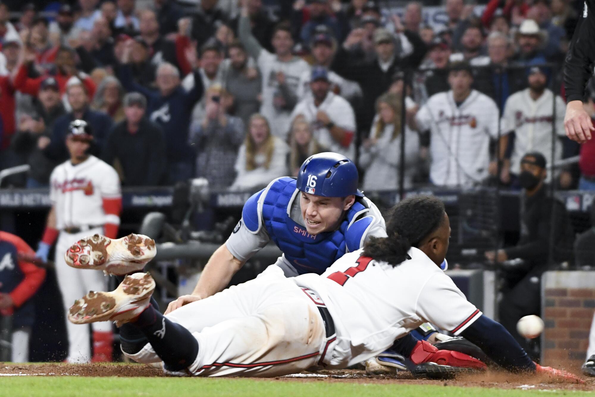 Atlanta Braves' Ozzie Albies, front, scores a run as Los Angeles Dodgers catcher Will Smith is unable to handle the pass 