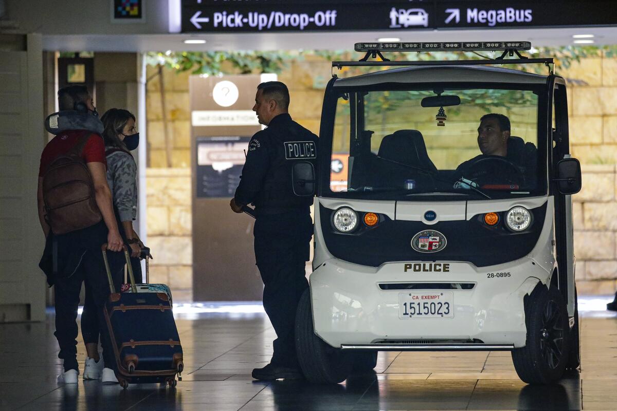 A police officer talks to two travelers while another man sits in a police vehicle.