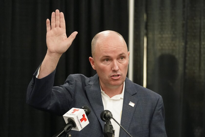 A man in a suit raises in his hand as he stands before microphones