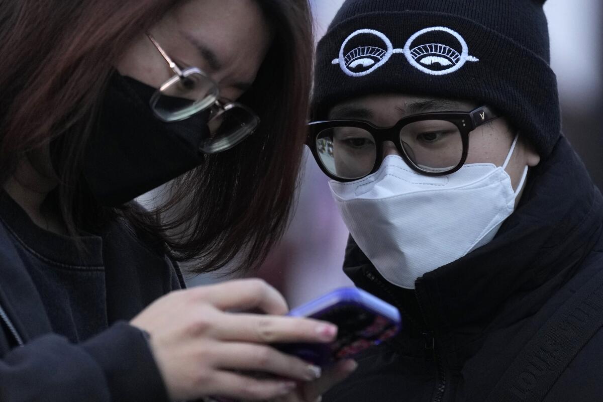 Two people wearing masks look at a phone together 