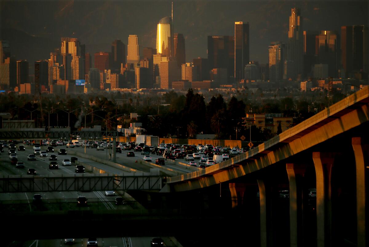 Cars fill freeway lanes. In the background is the smog-filled L.A. skyline.