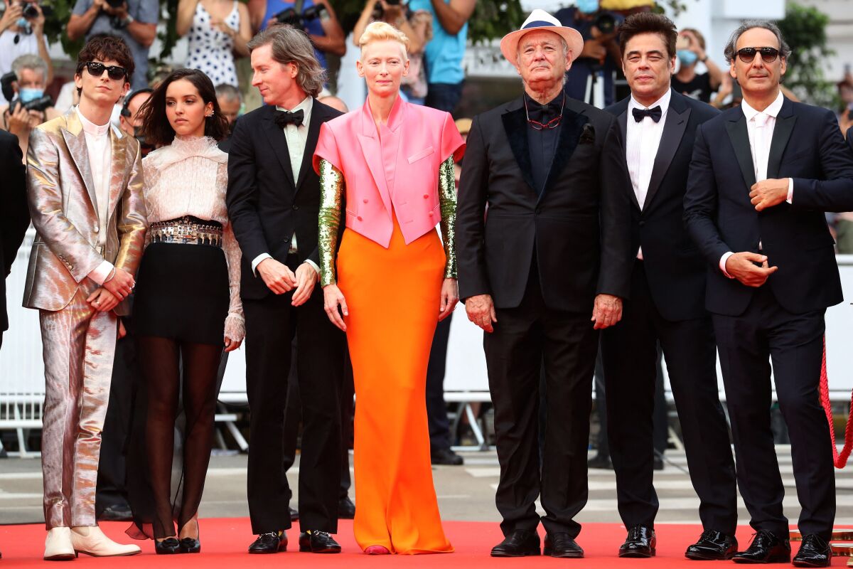 Seven people dressed in formalwear stand on a red carpet