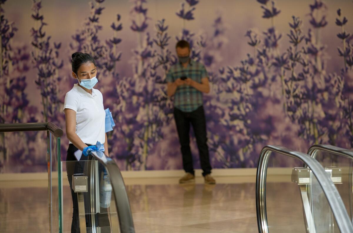 An employee of South Coast Plaza wipes handrails down with disinfectant on Monday.