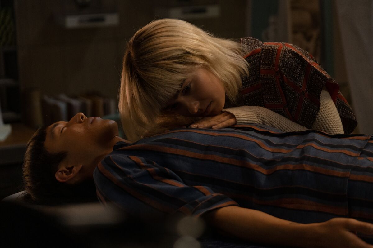 A woman rests her hand an ear on a man lying down