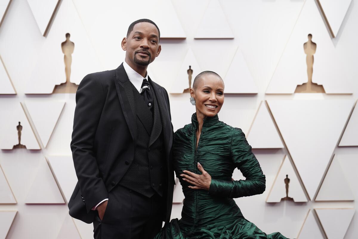 Will Smith in a black suit and tie and Jada Pinkett Smith in a green long-sleeved dress