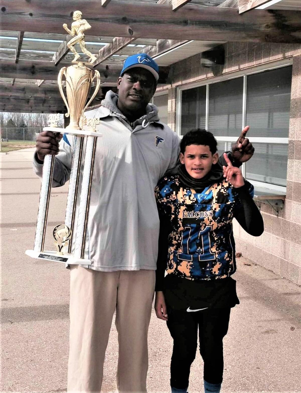 Otha Moore Sr. and Dante Moore pose while holding up a youth state championship trophy Dante's team won.