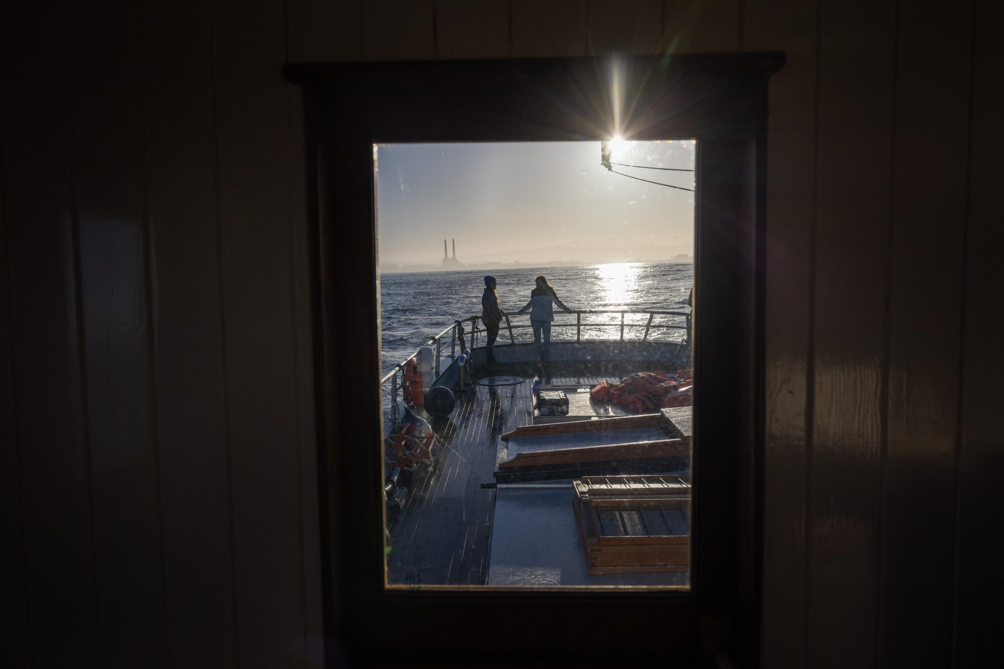 Two people are silhouetted as they stand at the rail at the stern of a boat.