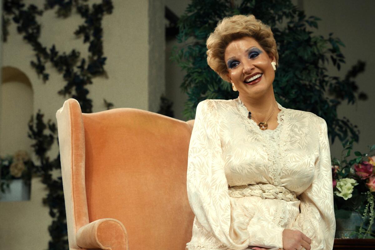 A woman in a chair smiles broadly in the film "The Eyes of Tammy Faye."