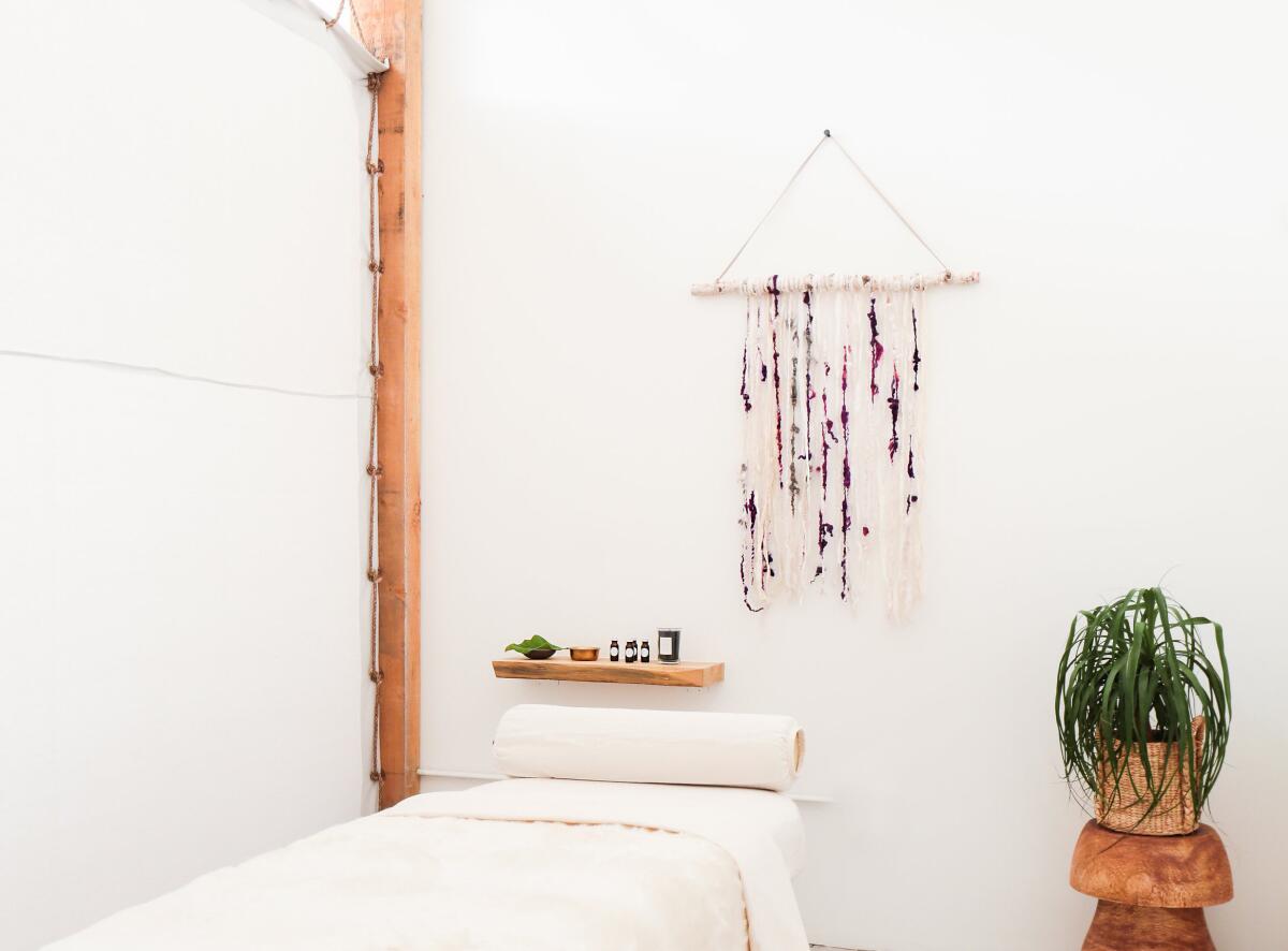 A massage table in a room with a wall hanging and a plant on a wooden stand.