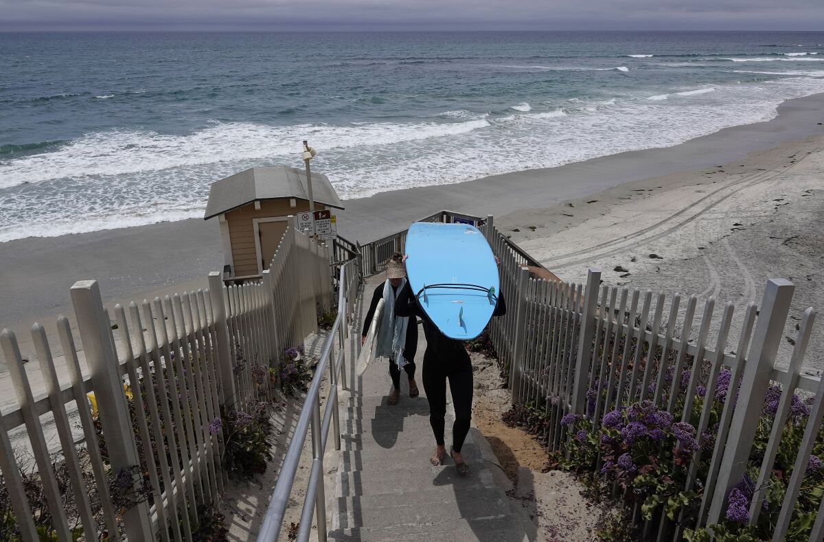 Surfers walk up the stairs at Tide Beach Park in Solana Beach on Tuesday, June 29, 2021.