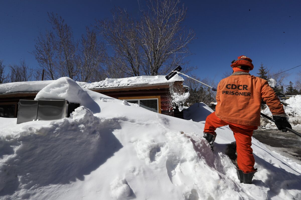 A Cal Fire Fenner Canyon fire inmate-crew member clears snow off the roof of a residence at a Big Bear Lake trailer park 