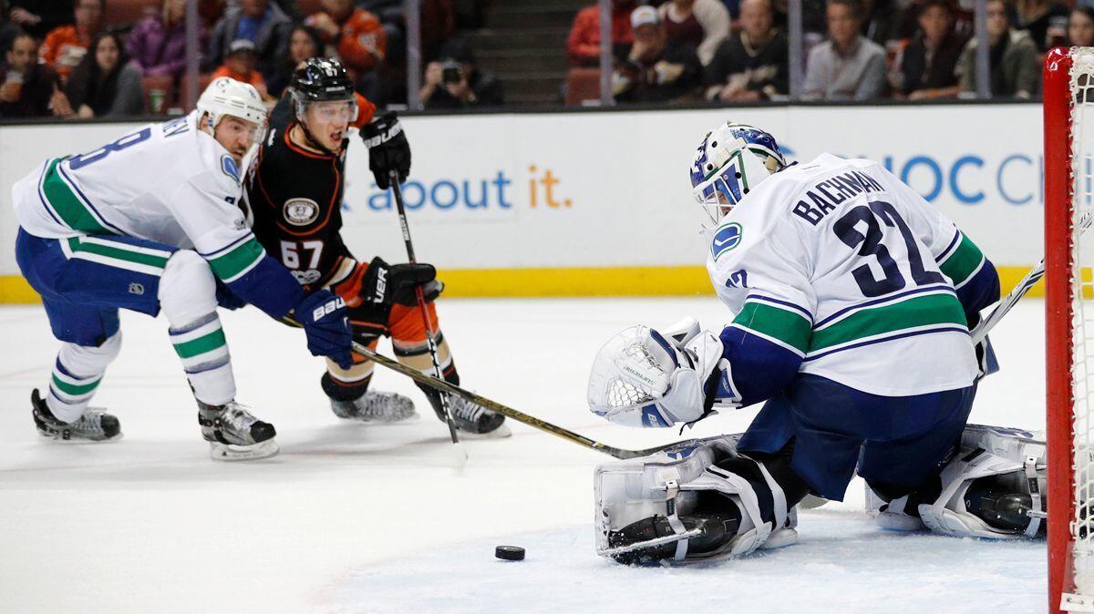 Vancouver Canucks goalie Richard Bachman, right, makes a save as teammate Christopher Tanev, left, and Ducks' Rickard Rakell watch during the second period Sunday.